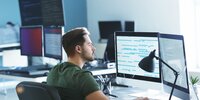 Programmierer arbeitet konzentriert am Computer mit mehreren Monitoren im modernen Büro.