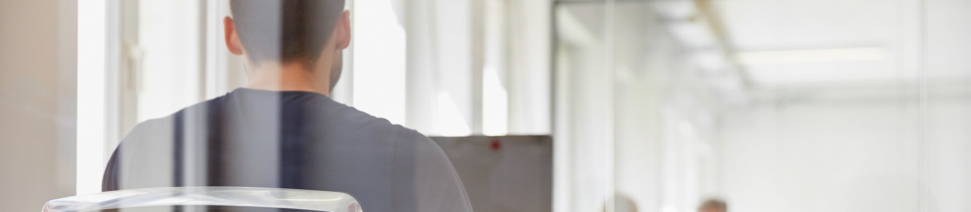 Mann in modernem Büro sitzt an einem Schreibtisch und arbeitet konzentriert hinter einer Glaswand.