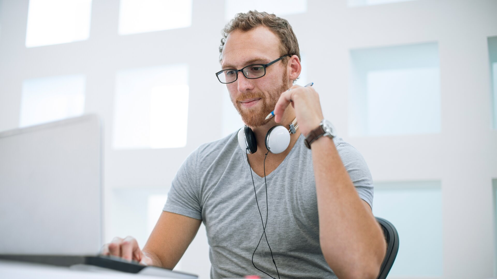 Hier ist ein geeigneter SEO-Alt-Tag-Satz für dieses Bild:  **„Mann mit Kopfhörern arbeitet konzentriert am Laptop in modernem, lichtdurchflutetem Büro.