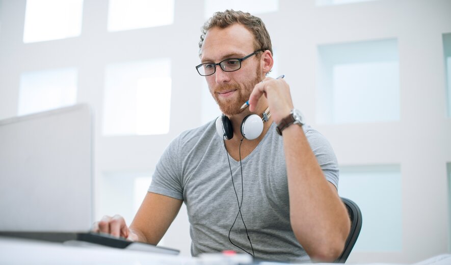 Hier ist ein geeigneter SEO-Alt-Tag-Satz für dieses Bild:  **„Mann mit Kopfhörern arbeitet konzentriert am Laptop in modernem, lichtdurchflutetem Büro.