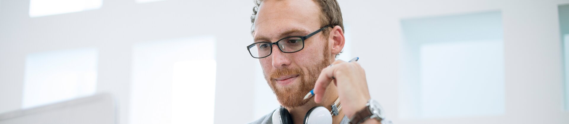 Hier ist ein geeigneter SEO-Alt-Tag-Satz für dieses Bild:  **„Mann mit Kopfhörern arbeitet konzentriert am Laptop in modernem, lichtdurchflutetem Büro.