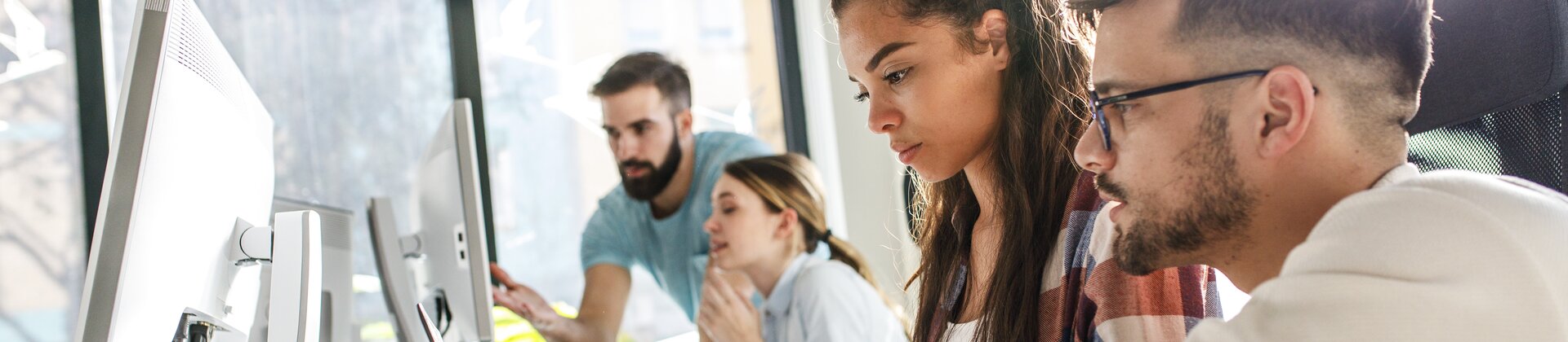 Team junger Professionals arbeitet gemeinsam an Computern in modernem Büro
