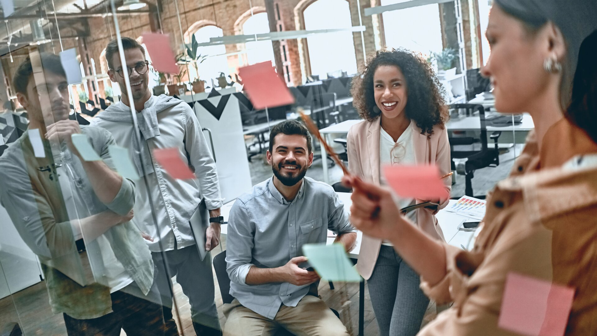 Team brainstormt in modernem Büro an einer Glaswand mit bunten Sticky Notes.