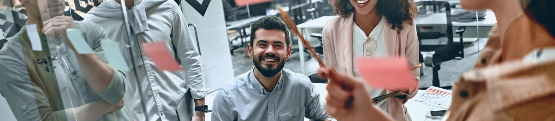 Team brainstormt in modernem Büro an einer Glaswand mit bunten Sticky Notes.