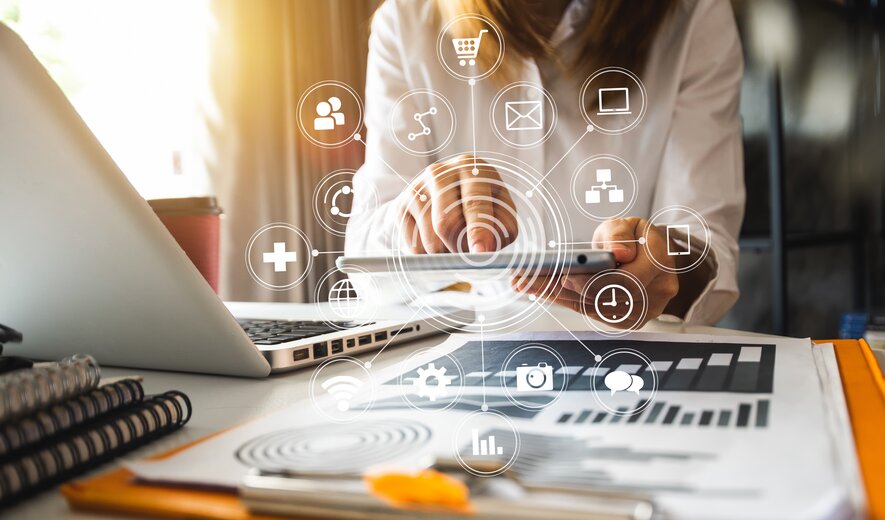 Eine Person arbeitet digital vernetzt mit Tablet und Laptop an Marketing- und Analyseprozessen.