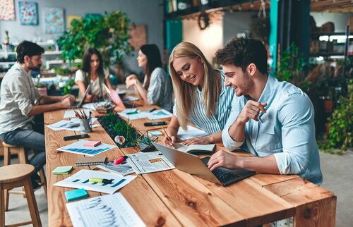 Team arbeitet gemeinsam an Laptop und Unterlagen – spiegelt nachhaltiges Handeln, Fairness und Zusammenhalt in der gGmbH der IHK Akademie München und Oberbayern wider.