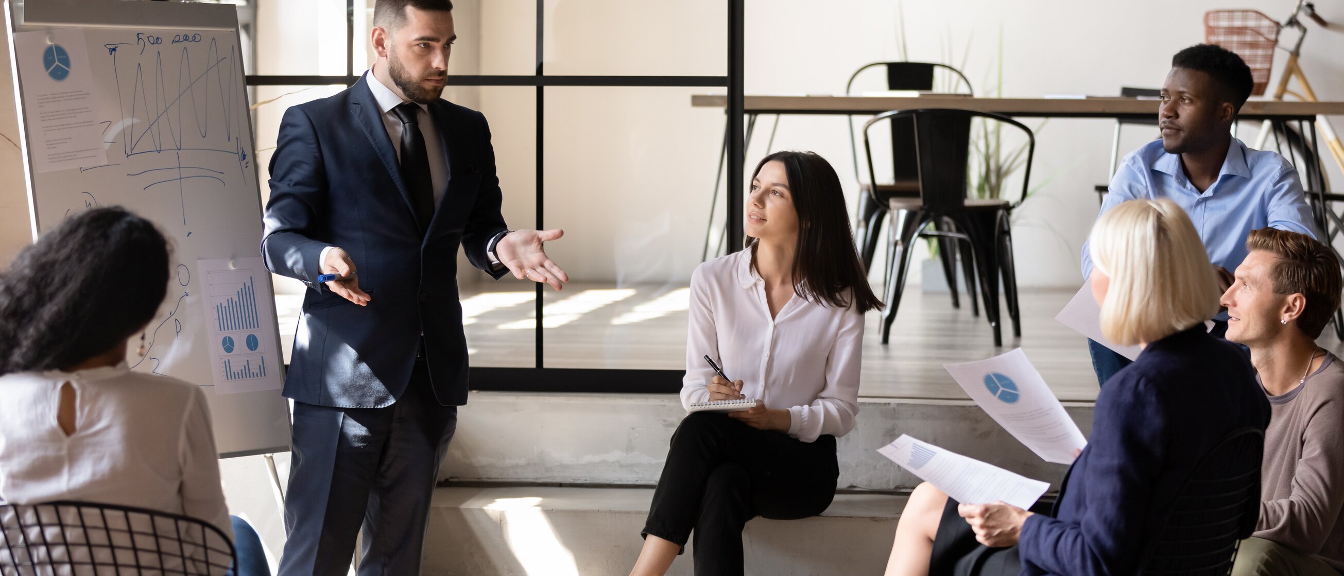 Ein Trainer erklärt einer Gruppe von Teilnehmenden in einer Vertriebs-Weiterbildung der IHK Akademie München erfolgreiche Strategien zur Kundenbindung und Umsatzsteigerung.