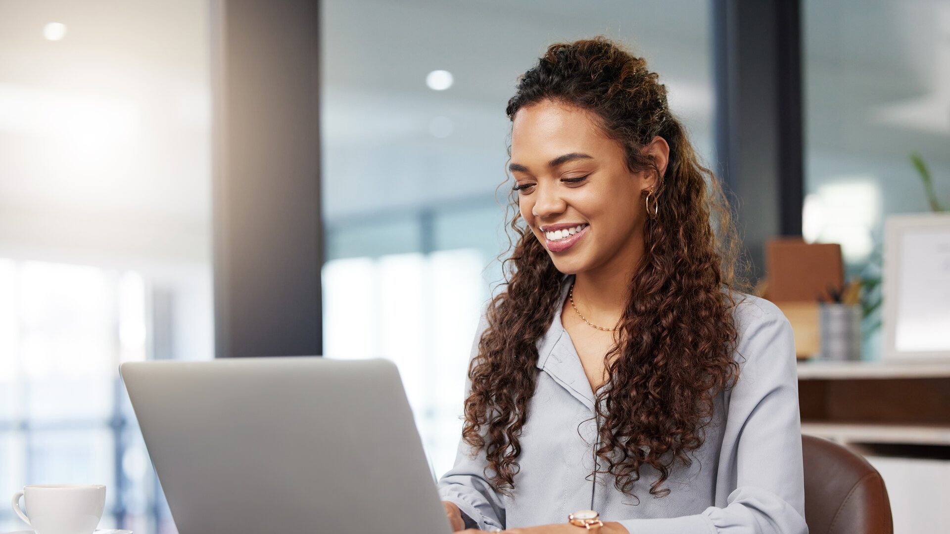 Junge Frau arbeitet lächelnd am Laptop in modernem Büro