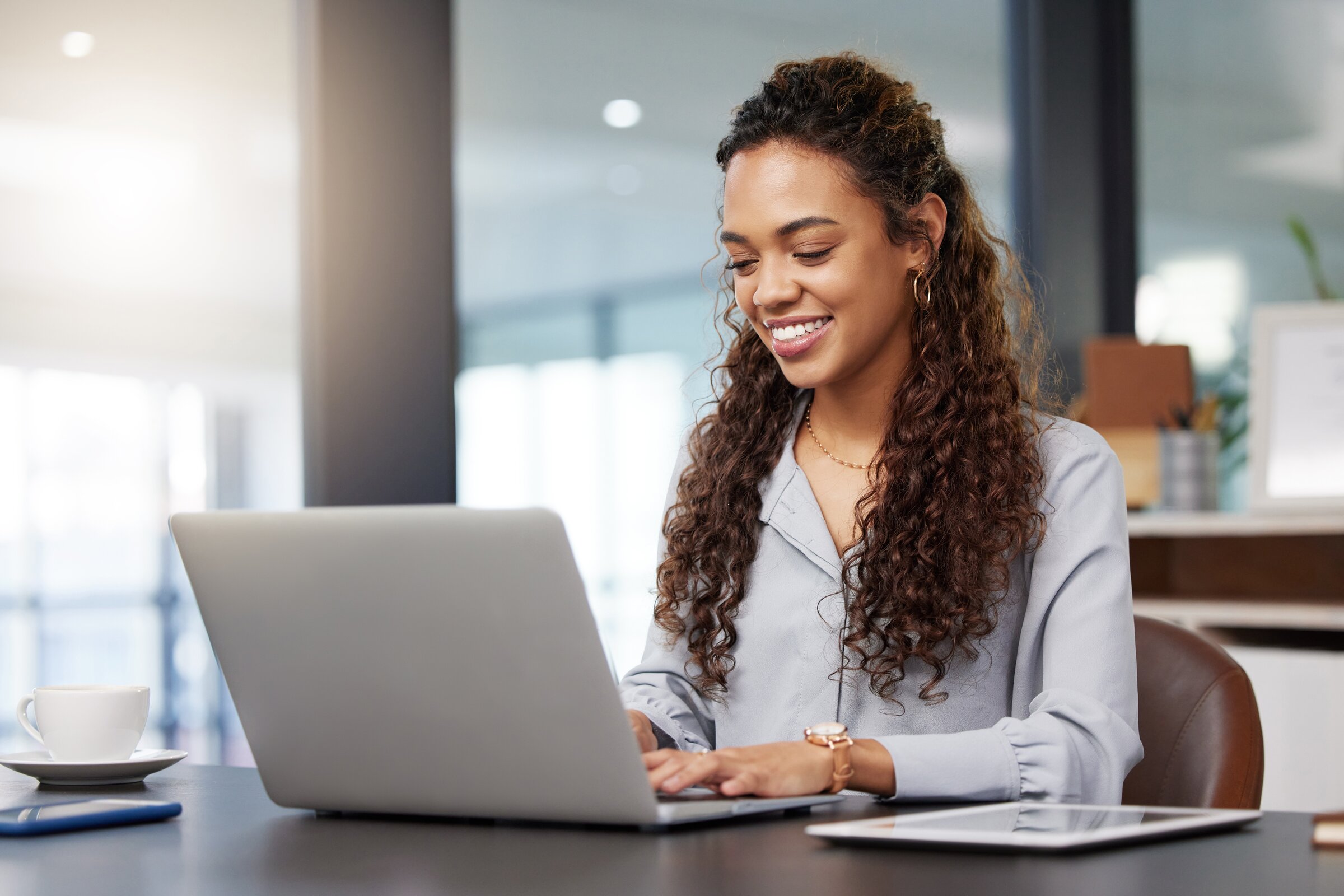 Junge Frau arbeitet lächelnd am Laptop in modernem Büro