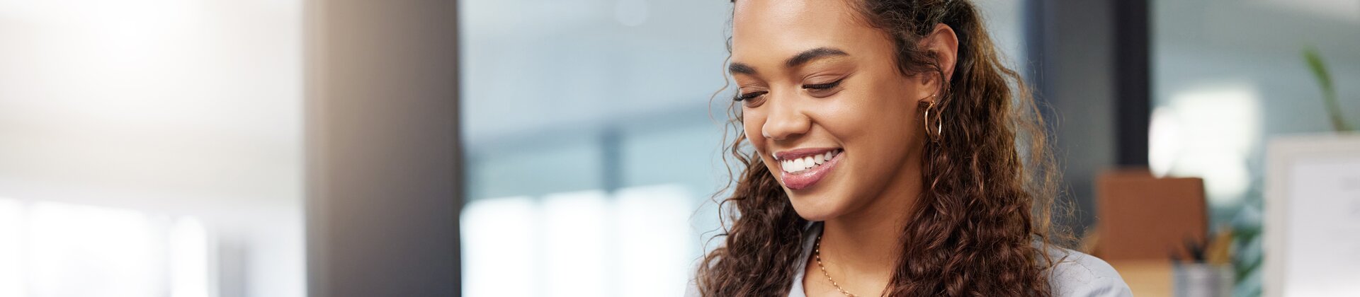 Junge Frau arbeitet lächelnd am Laptop in modernem Büro