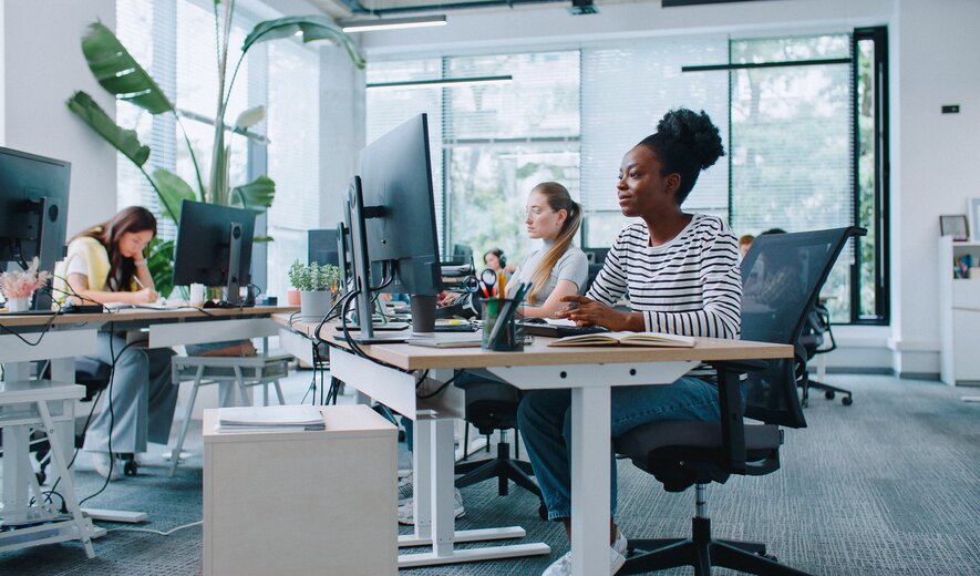 Moderne Büroarbeitsplätze mit mehreren Mitarbeitern an Computerarbeitsplätzen in einem offenen, hellen Office