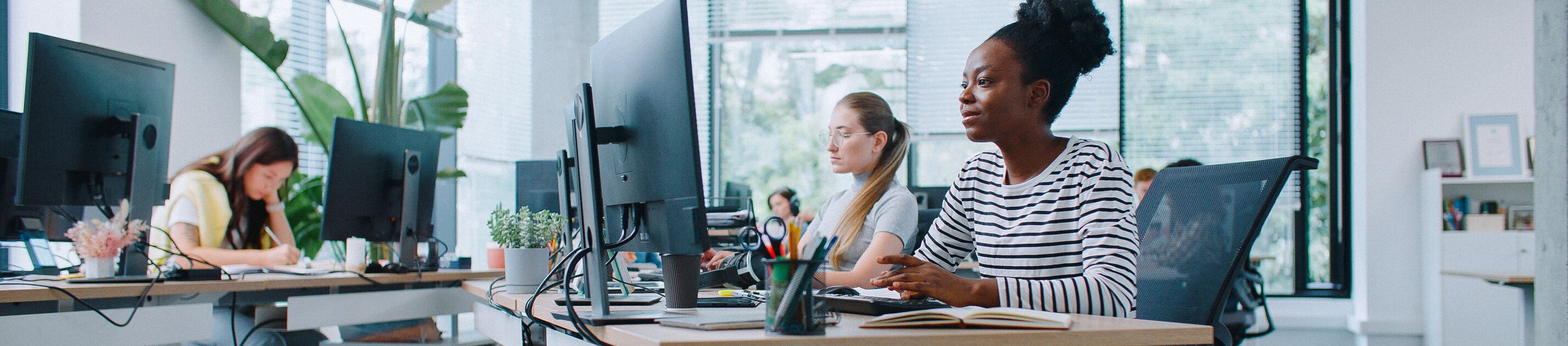 Moderne Büroarbeitsplätze mit mehreren Mitarbeitern an Computerarbeitsplätzen in einem offenen, hellen Office
