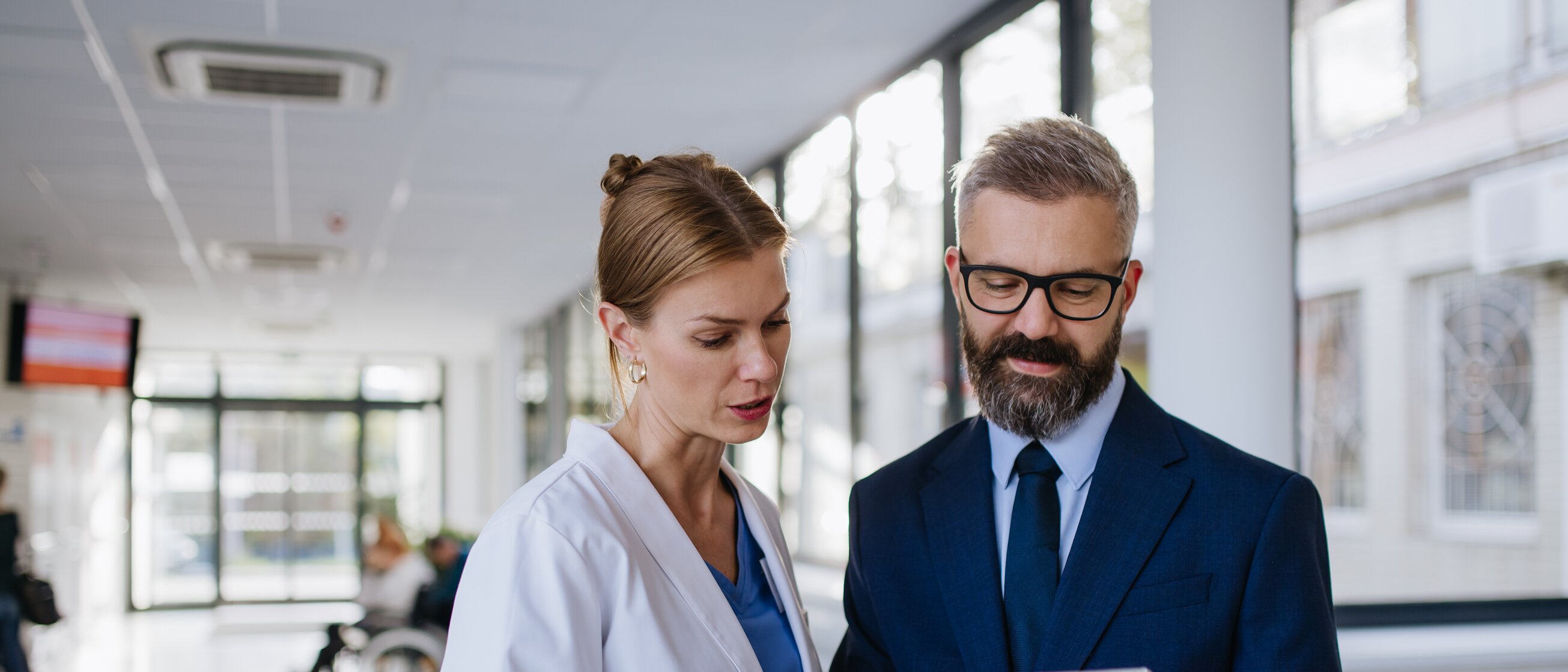 Eine Ärztin und ein Manager besprechen Gesundheitsdaten auf einem Tablet – Sinnbild für Weiterbildungen im Gesundheitsmanagement, die Mitarbeitendenwohl und nachhaltigen Unternehmenserfolg fördern.