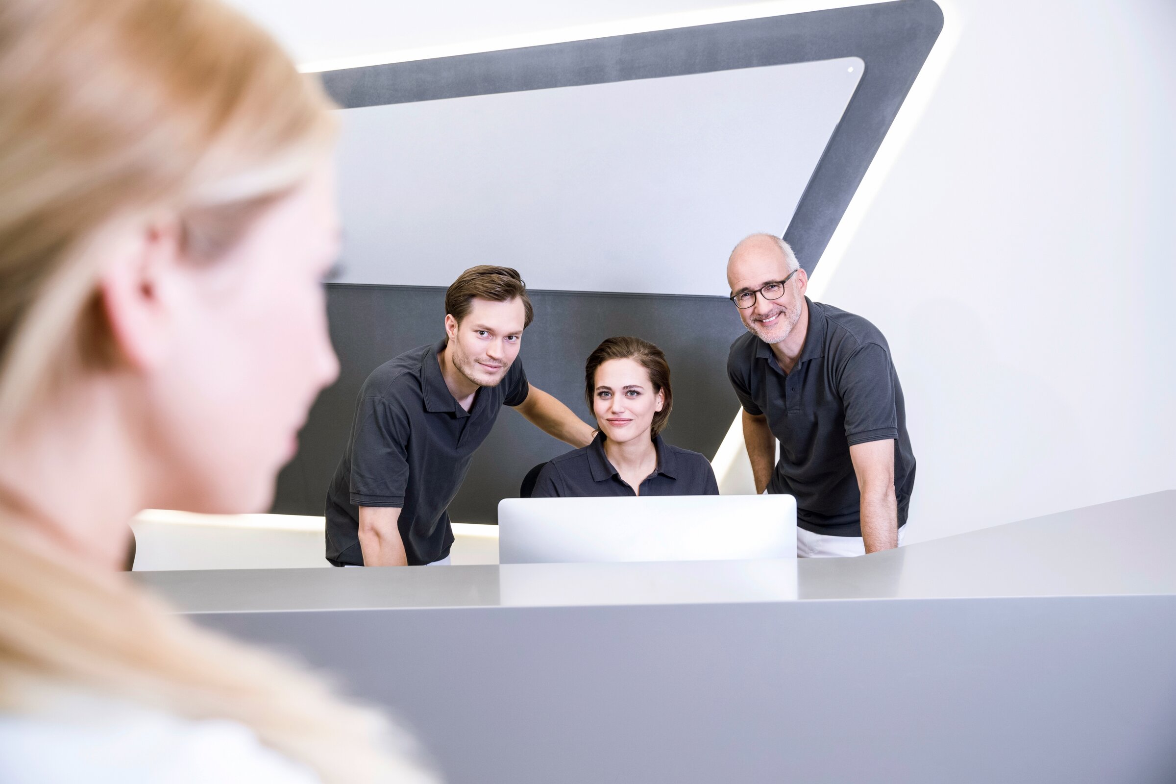 Weiterbildung im Gesundheitsweisen: Ein Praxisteam steht hinter dem Empfang und begrüßt eine Patentin.