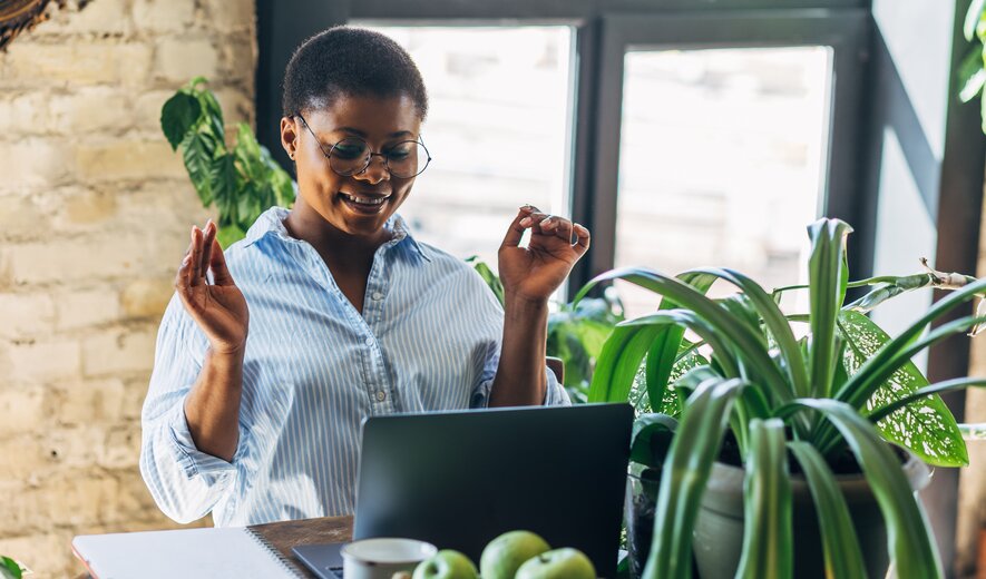Frau arbeitet lächelnd am Laptop in heller, pflanzenreicher Umgebung