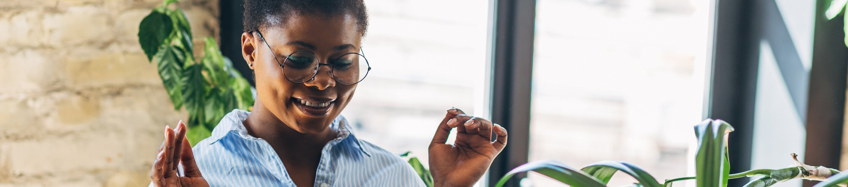 Frau arbeitet lächelnd am Laptop in heller, pflanzenreicher Umgebung