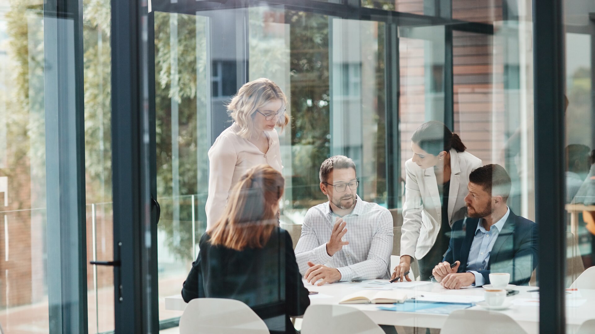 Teammeeting hinter Glaswand im modernen Büro.