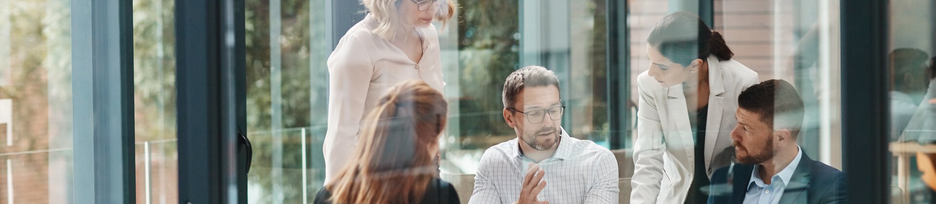 Teammeeting hinter Glaswand im modernen Büro.