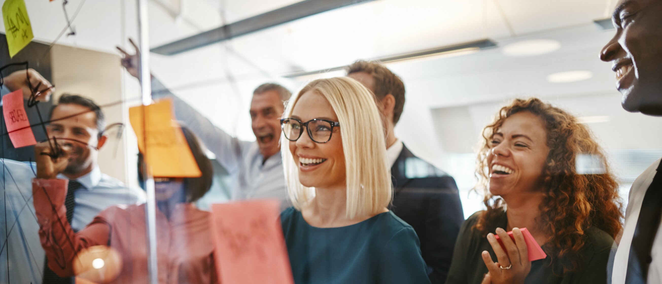 Ein motiviertes Projektteam arbeitet kreativ mit Post-its an einer Glaswand während einer Weiterbildung im Projektmanagement an der IHK Akademie Westerham.