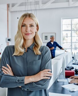Projektleiterin steht vor einem Tisch, an dem ihr Team sitzt und an einem Projekt arbeitet. 