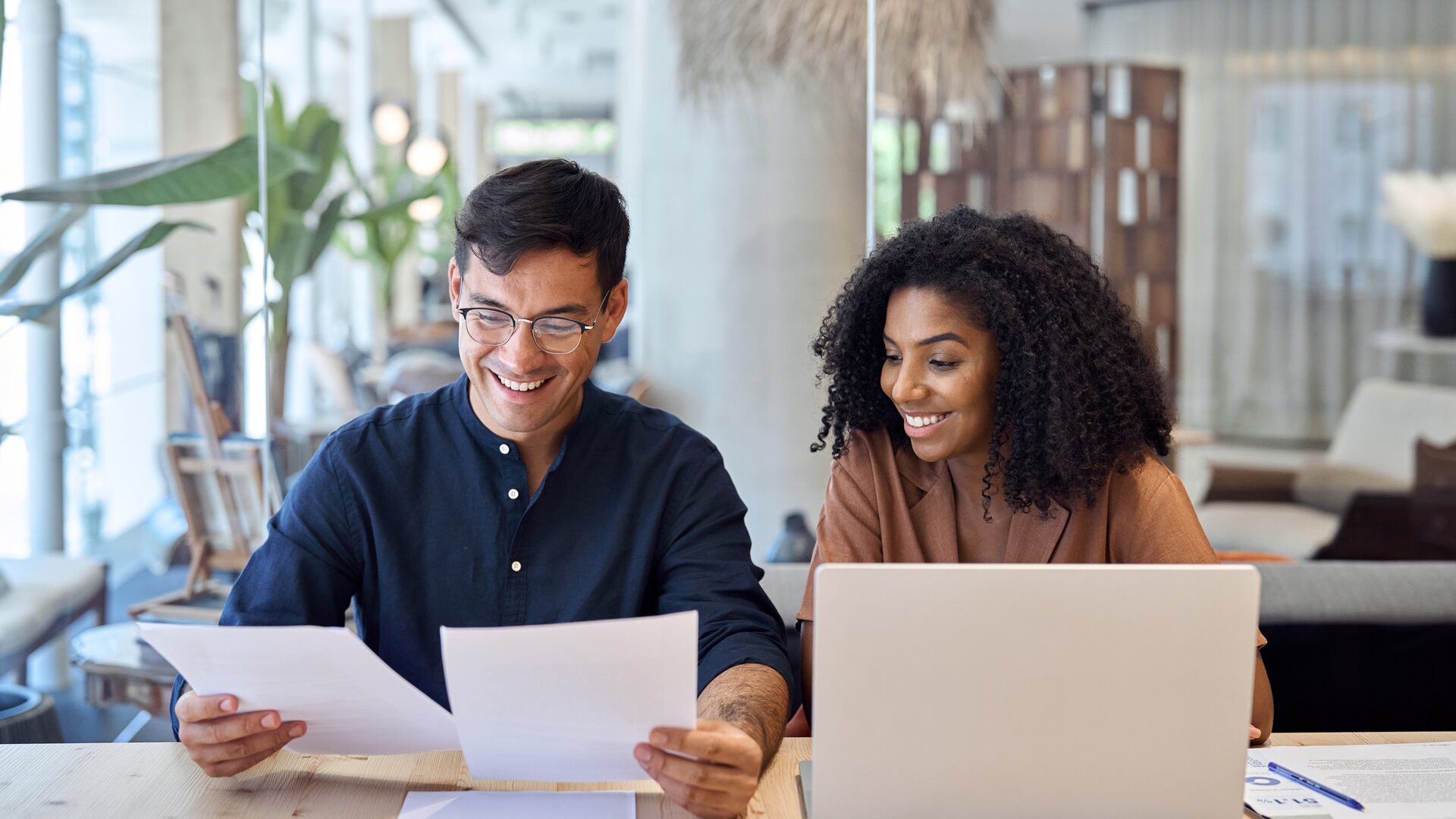 Zwei junge Berufstätige arbeiten gemeinsam am Laptop und analysieren Dokumente in modernem Büro