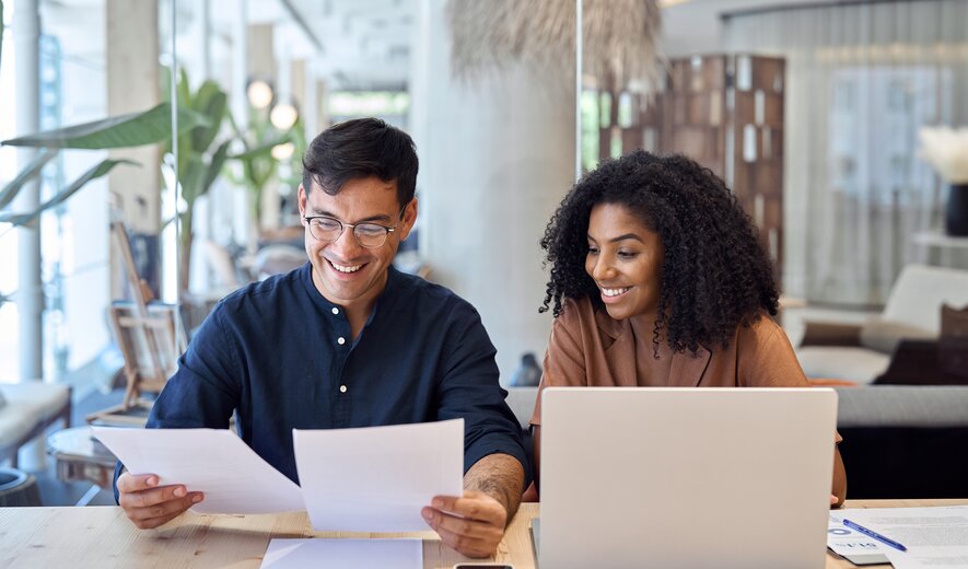 Zwei junge Berufstätige arbeiten gemeinsam am Laptop und analysieren Dokumente in modernem Büro