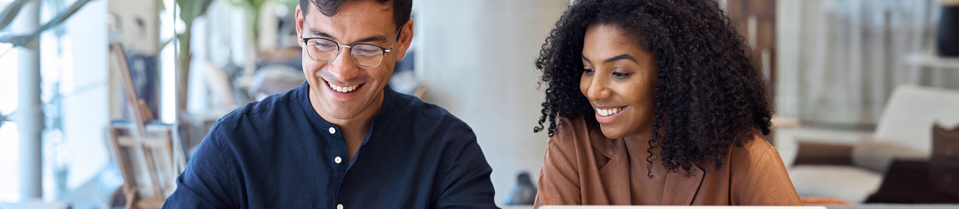 Zwei junge Berufstätige arbeiten gemeinsam am Laptop und analysieren Dokumente in modernem Büro