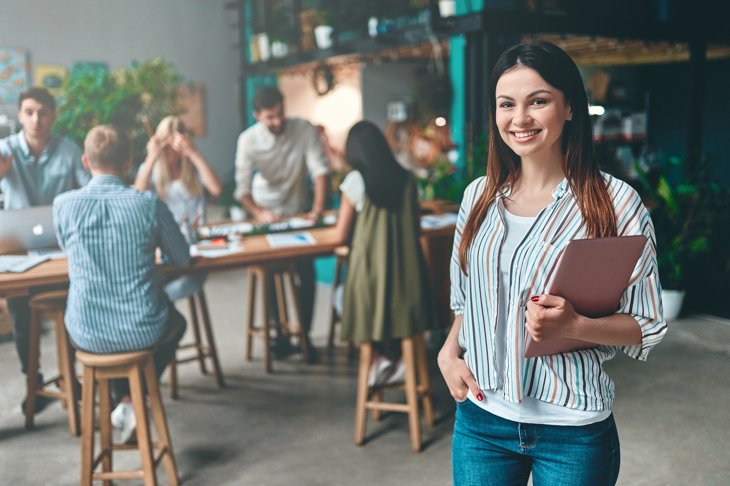 Junge Frau mit Tablet steht lächelnd in modernem Büro – Symbolbild für die Weiterbildung Projektmanager/-in IHK an der IHK Akademie Ingolstadt