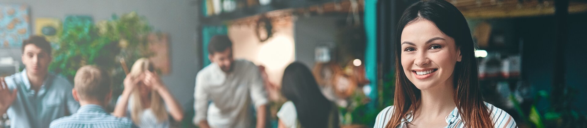 Weiterbildung im Projektmanagement: Junge Dame steht im Vordergrund eines Raumes und schaut direkt in die Kamera. 