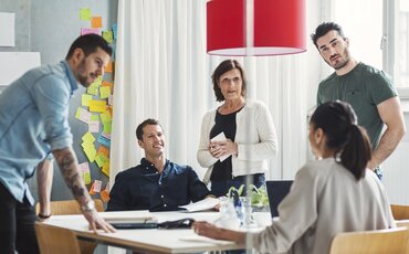 Projektleiter diskutiert mit Projektteam an einem Meetingtisch. 