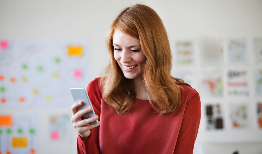 lächelnde frau im büro schaut aufs smartphone