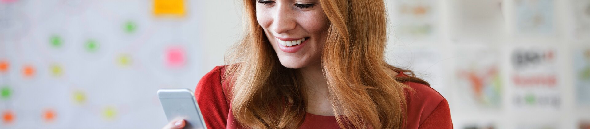 lächelnde frau im büro schaut aufs smartphone