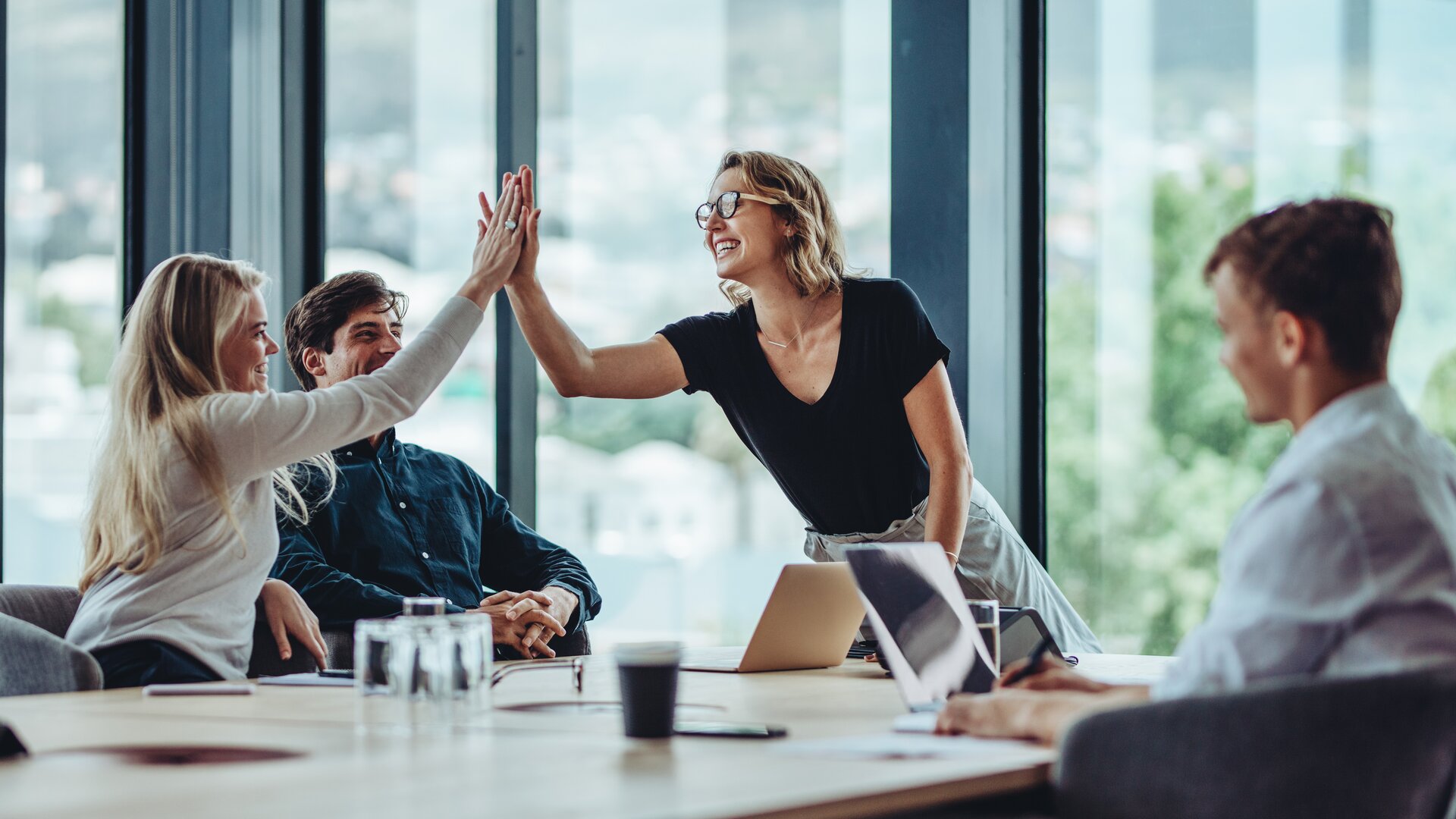 team jubelt beim erfolgreichen projektmeeting und gibt sich ein high five im modernen büro