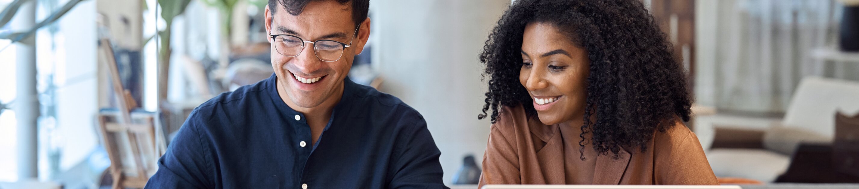 Zwei junge Berufstätige arbeiten gemeinsam am Laptop und analysieren Dokumente in modernem Büro