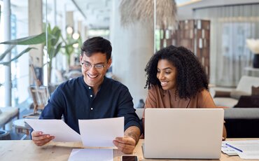 Junge Projektmanagerin präsentiert ein Konzept in einem modernen Büro, während ihr Team im Hintergrund an Projektstrategien arbeitet – Weiterbildung im Projektmanagement an der IHK Akademie.