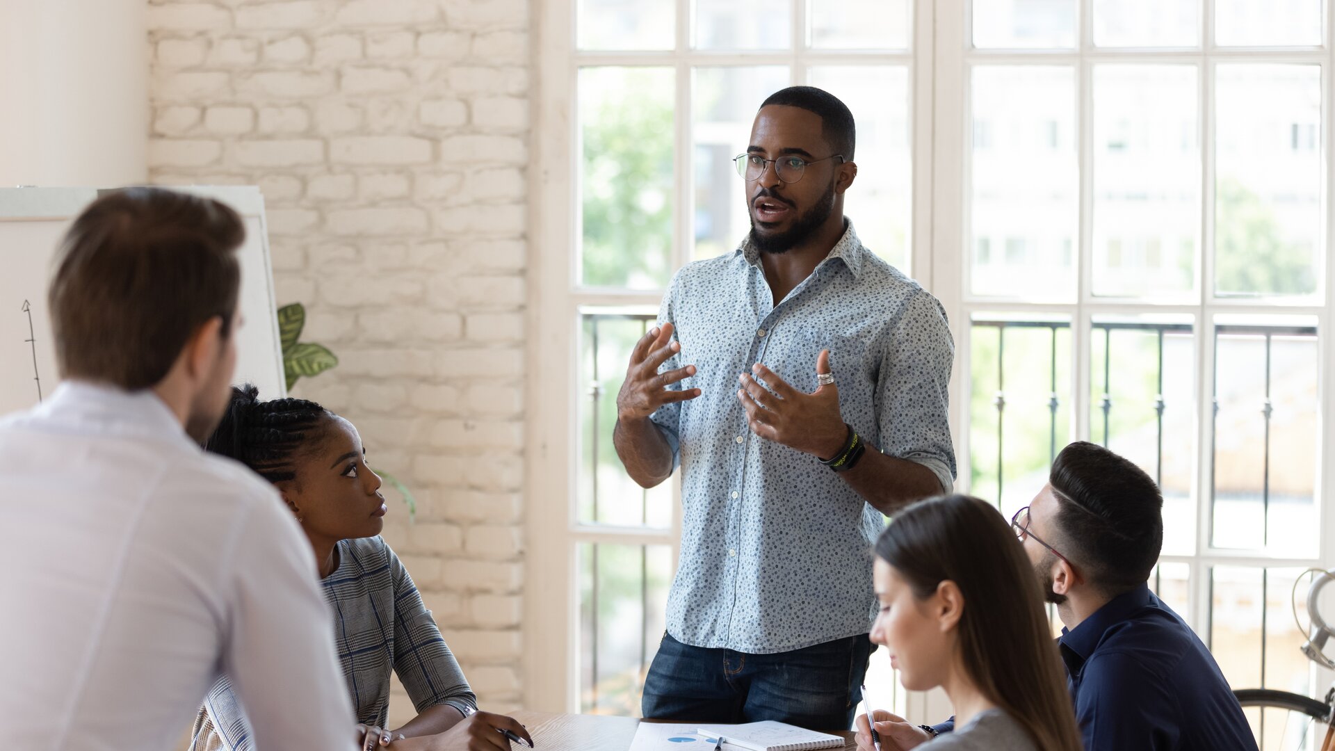 Teammeeting in modernem Büro, Mitarbeiter präsentiert Ideen vor Kolleginnen und Kollegen