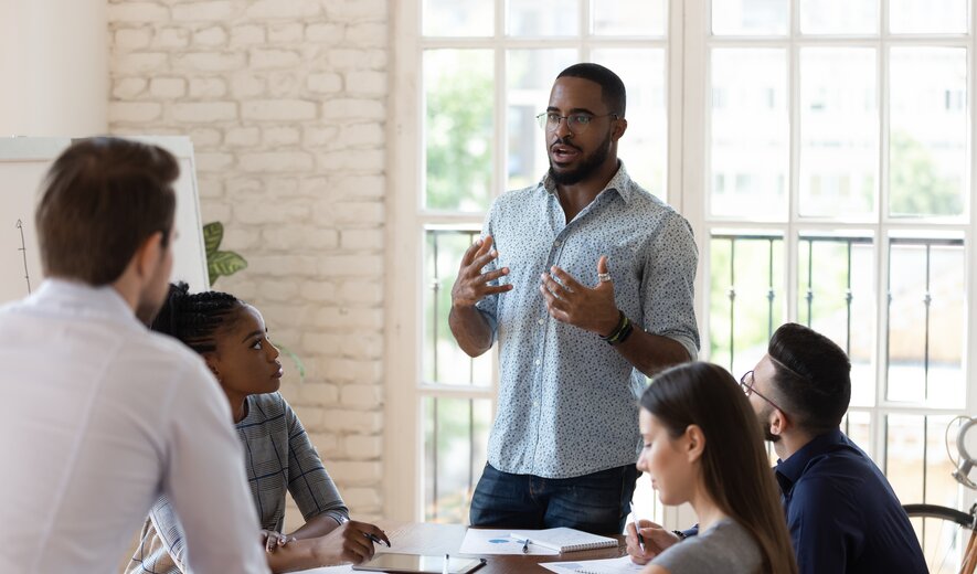 Teammeeting in modernem Büro, Mitarbeiter präsentiert Ideen vor Kolleginnen und Kollegen