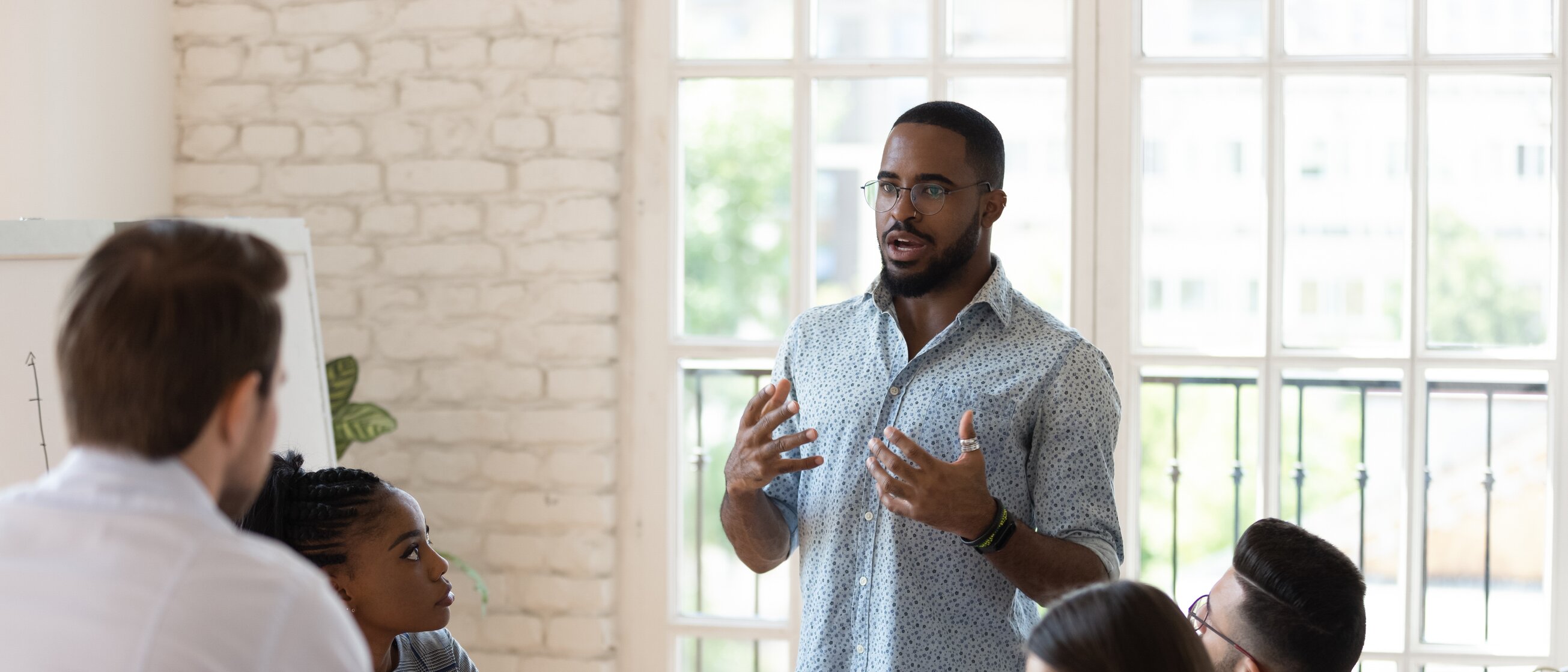 Trainer spricht engagiert zu seinem Team während einer Besprechung – praxisorientierte Weiterbildung für effizientes Arbeiten, klare Kommunikation und Führungskompetenz im Berufsalltag.