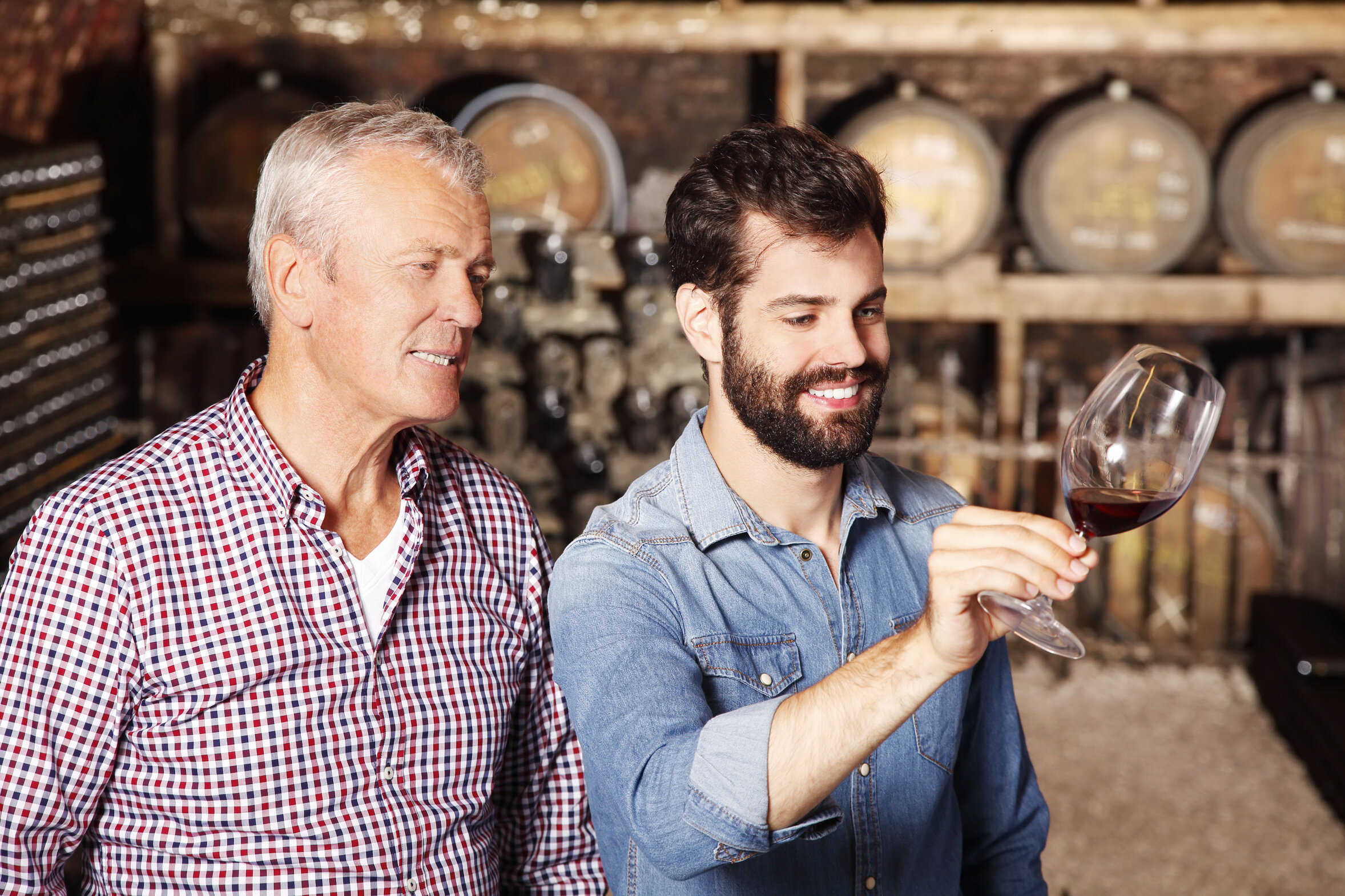 Zwei Winzer verkosten Rotwein im Weinkeller und beurteilen Farbe und Qualität.