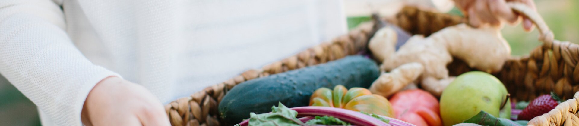 Person hält einen Korb mit frischem Gemüse wie Paprika, Roter Bete, Gurke und Äpfeln im Garten