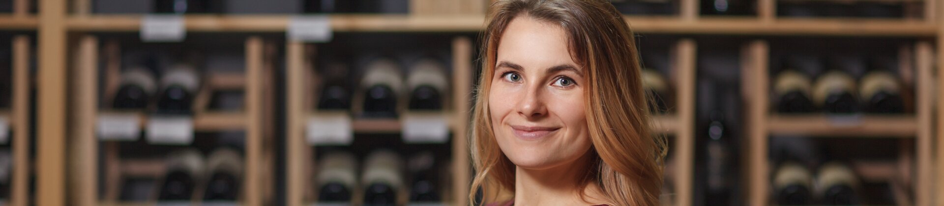 Lächelnde Sommelière steht vor einem Weinregal in einer Vinothek