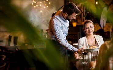 Mann berät eine Frau im Restaurant – praxisnahe Weiterbildung in Gastronomie und Servicekompetenz für Fachkräfte, die Gästeerlebnisse professionell gestalten möchten.