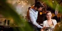 Kellner serviert lächelnder Frau ein Gericht in einem stilvollen Restaurant – freundlicher Service und angenehme Atmosphäre