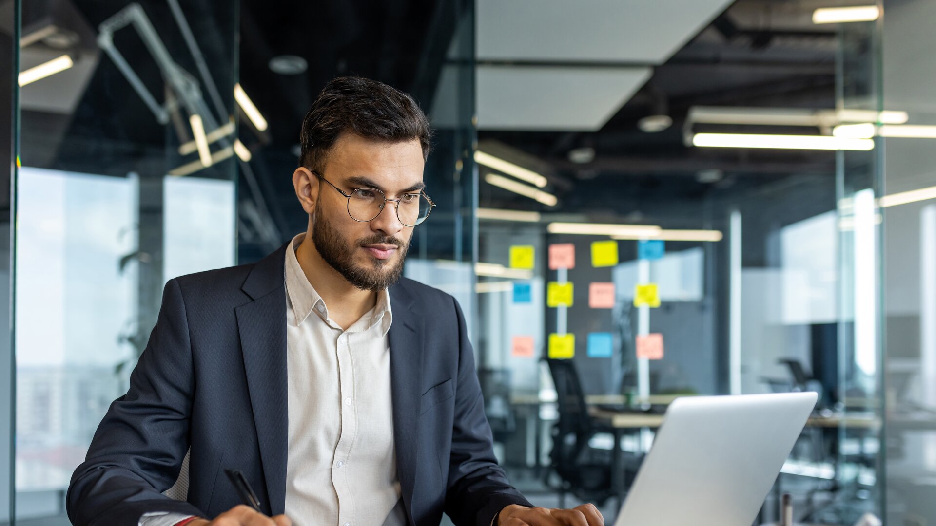 Businessman working on laptop in modern office, analysing documents and data