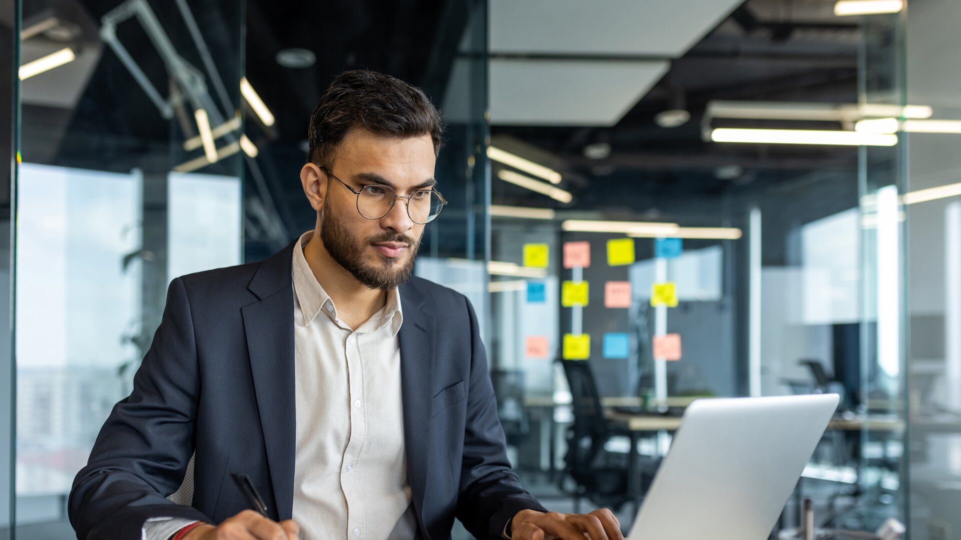 Businessman working on laptop in modern office, analysing documents and data