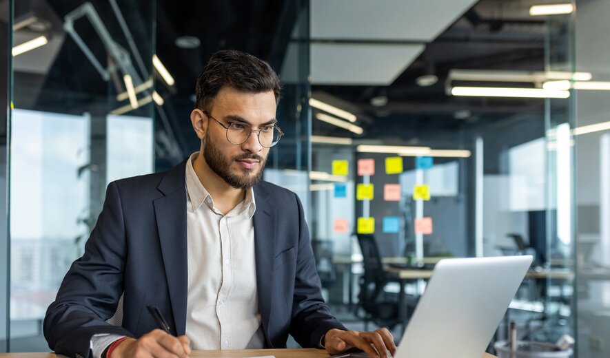Businessman working on laptop in modern office, analysing documents and data