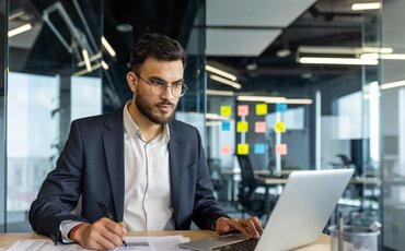 Geschäftsperson analysiert Dokumente und Zolltarife am Laptop – Weiterbildung zu Zolltarif, Steuern, Incoterms und internationalen Handelsvorschriften.