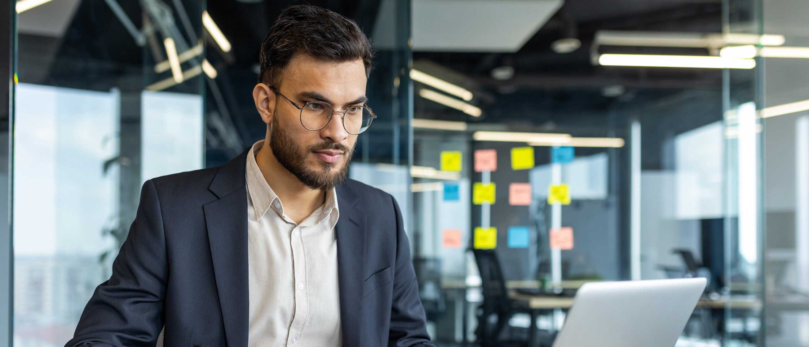 Ein junger Mann im Business-Outfit arbeitet konzentriert am Laptop in einem modernen Büro – Weiterbildung zu Warenursprung und Präferenzen im internationalen Handel.