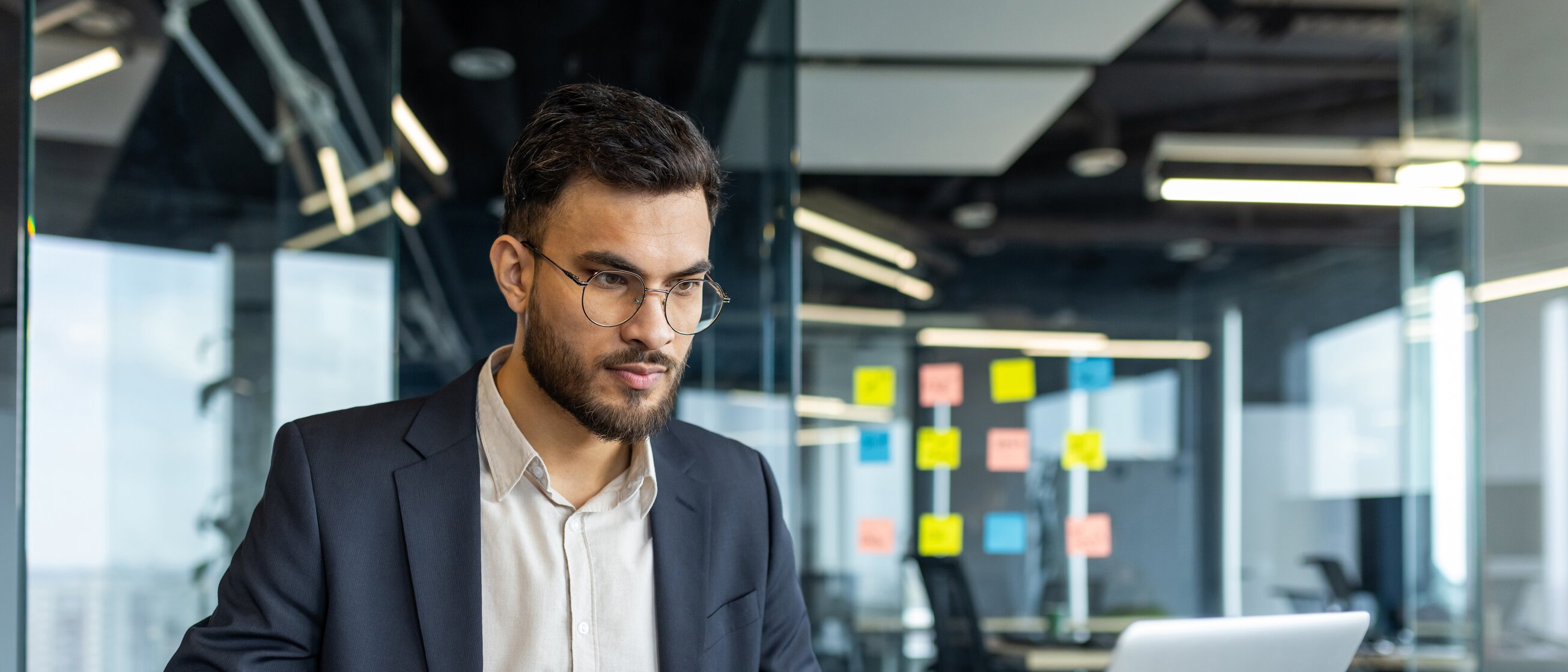 Ein junger Mann im Business-Outfit arbeitet konzentriert am Laptop in einem modernen Büro