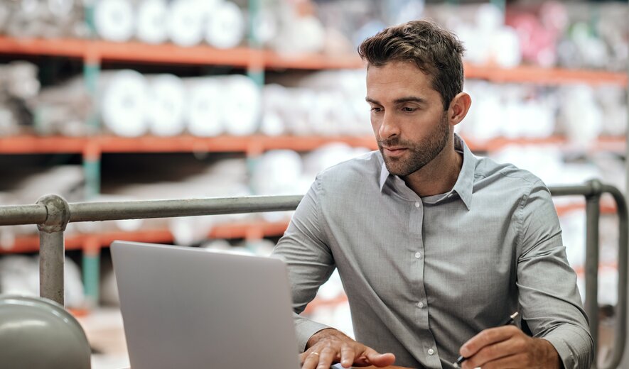 Mitarbeiter arbeitet im Lager an einem Laptop und erstellt Notizen